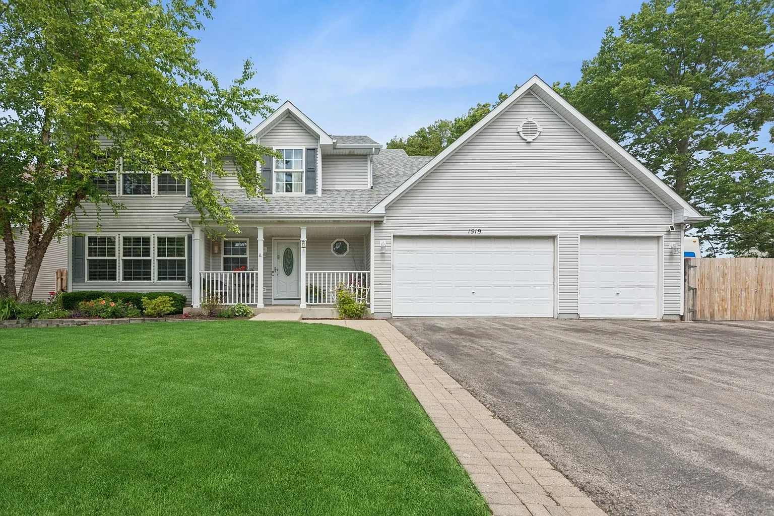 Two-story house with covered porch, double garage, grass, and trees.