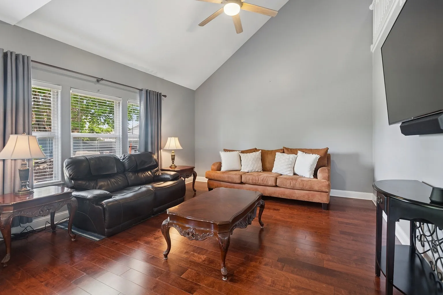 Living room with leather sofa, tan couch, coffee table, lamps, hardwood floors, and large windows.