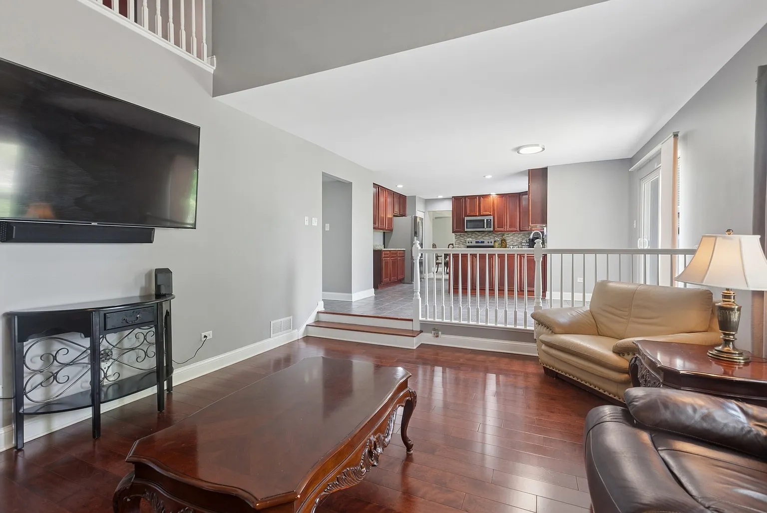 Living room with wall-mounted TV, coffee table, seating, wood floors, and open kitchen.