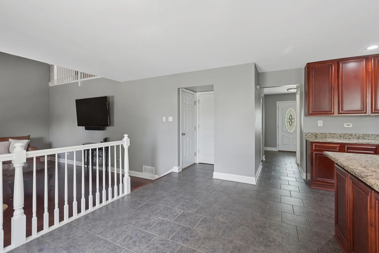 Living area and kitchen with gray walls, dark flooring, wood cabinets, TV, and staircase.