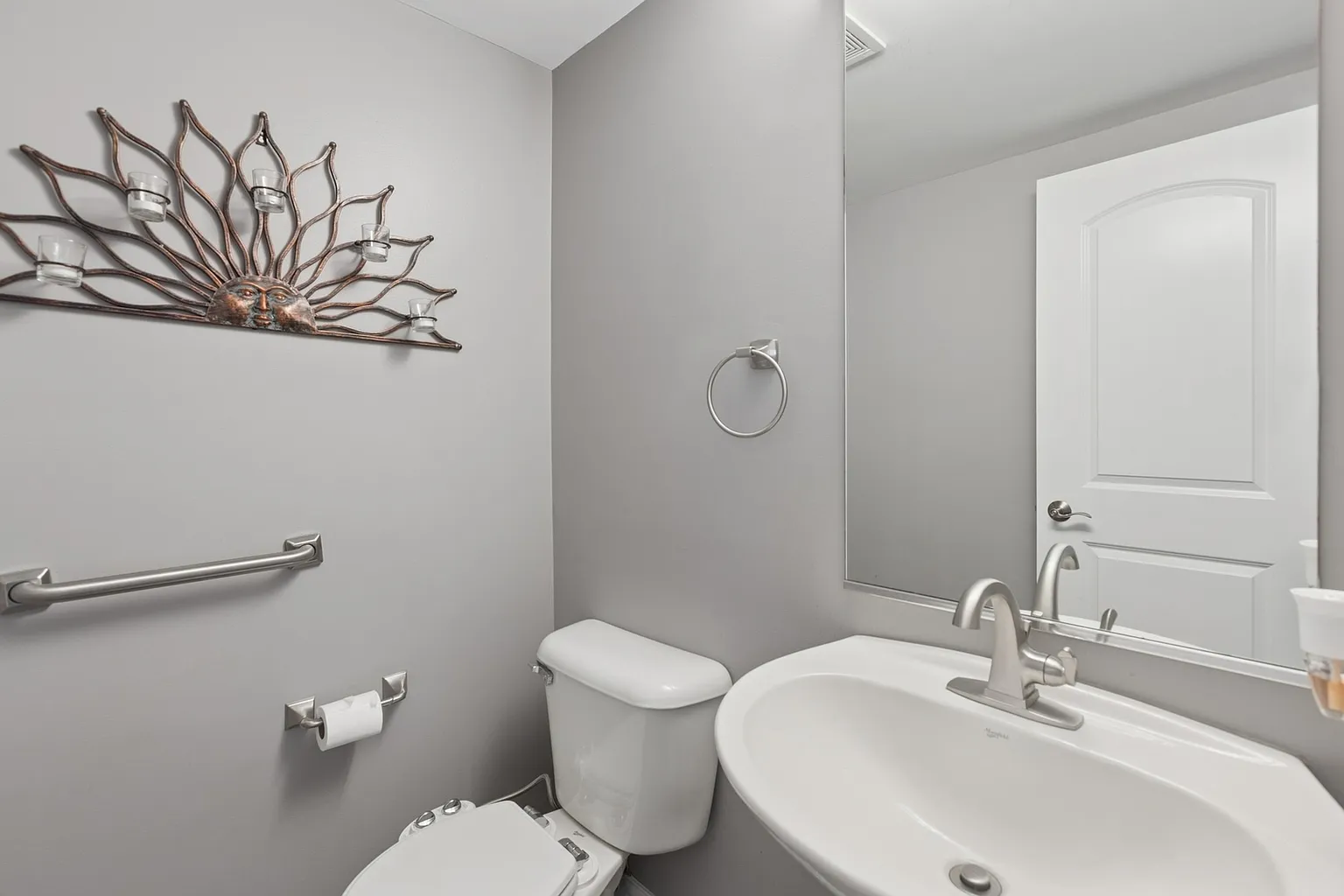 Small bathroom with toilet, sink, mirror, gray walls, towel bar, and light fixture.