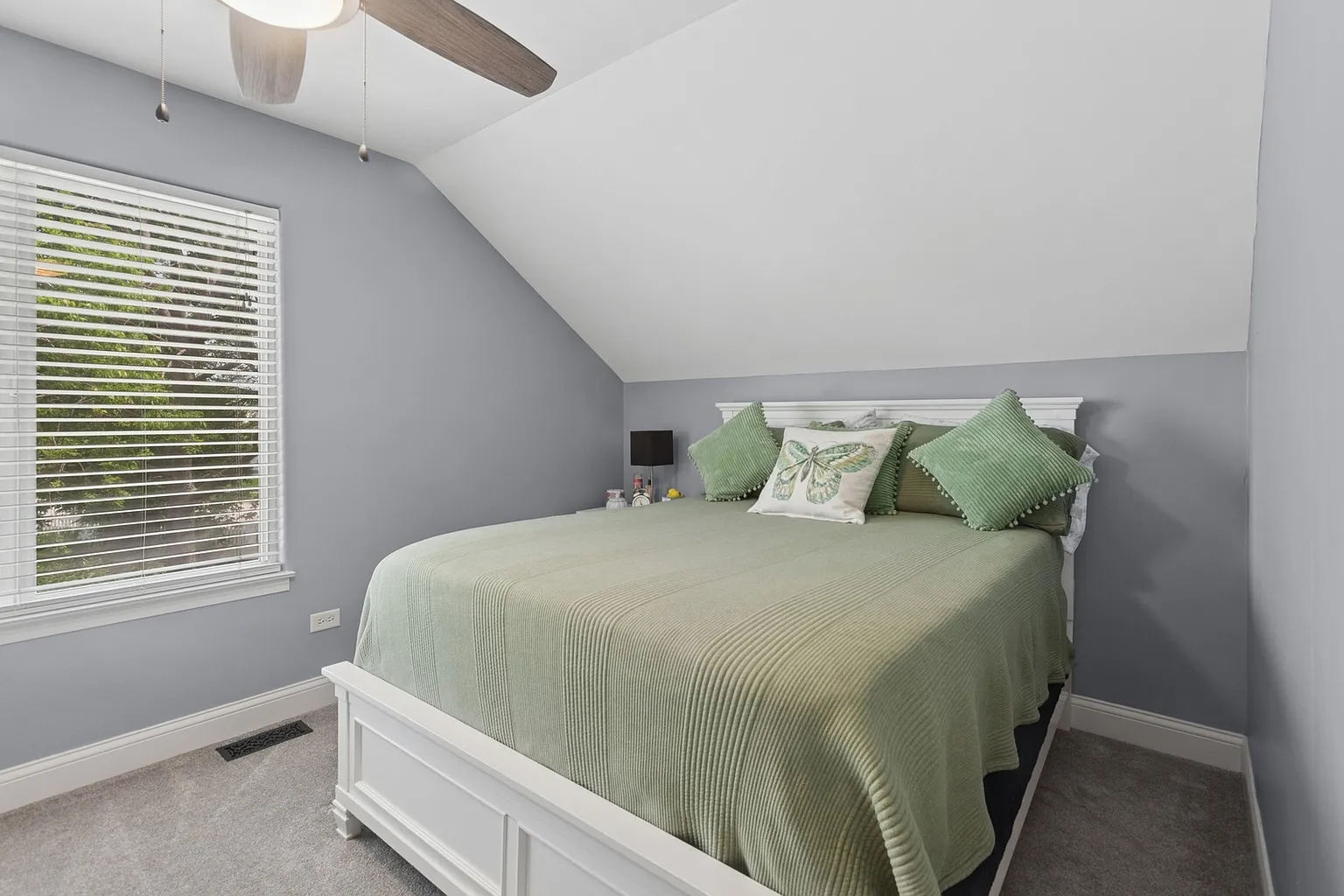 Cozy bedroom with slanted ceiling, queen bed, green blanket, and window blinds.