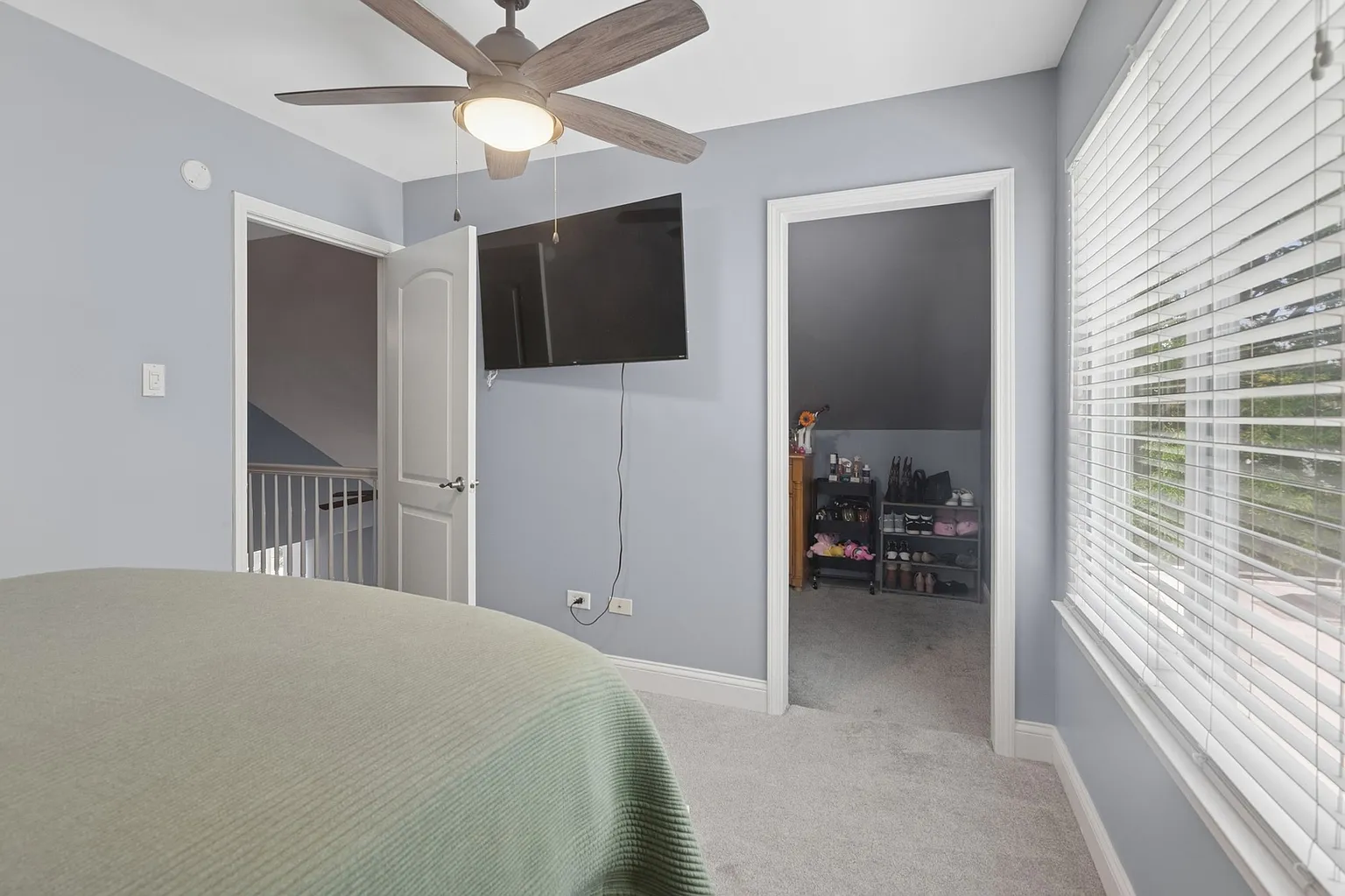 Bedroom corner with ceiling fan, wall-mounted TV, gray walls, and beige carpet.