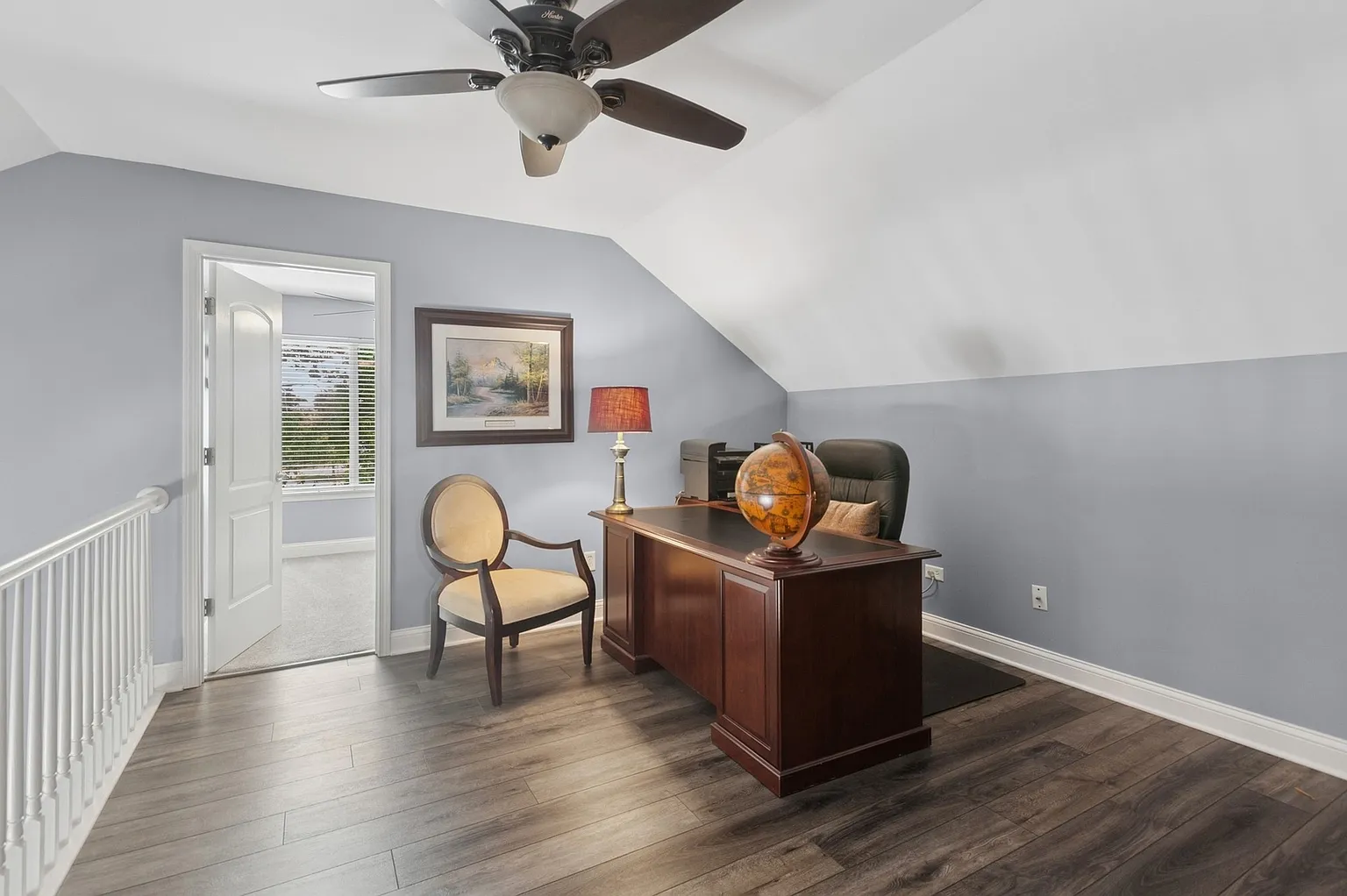 Tidy office with wooden desk, chair, orange lamp, globe, and large windows.