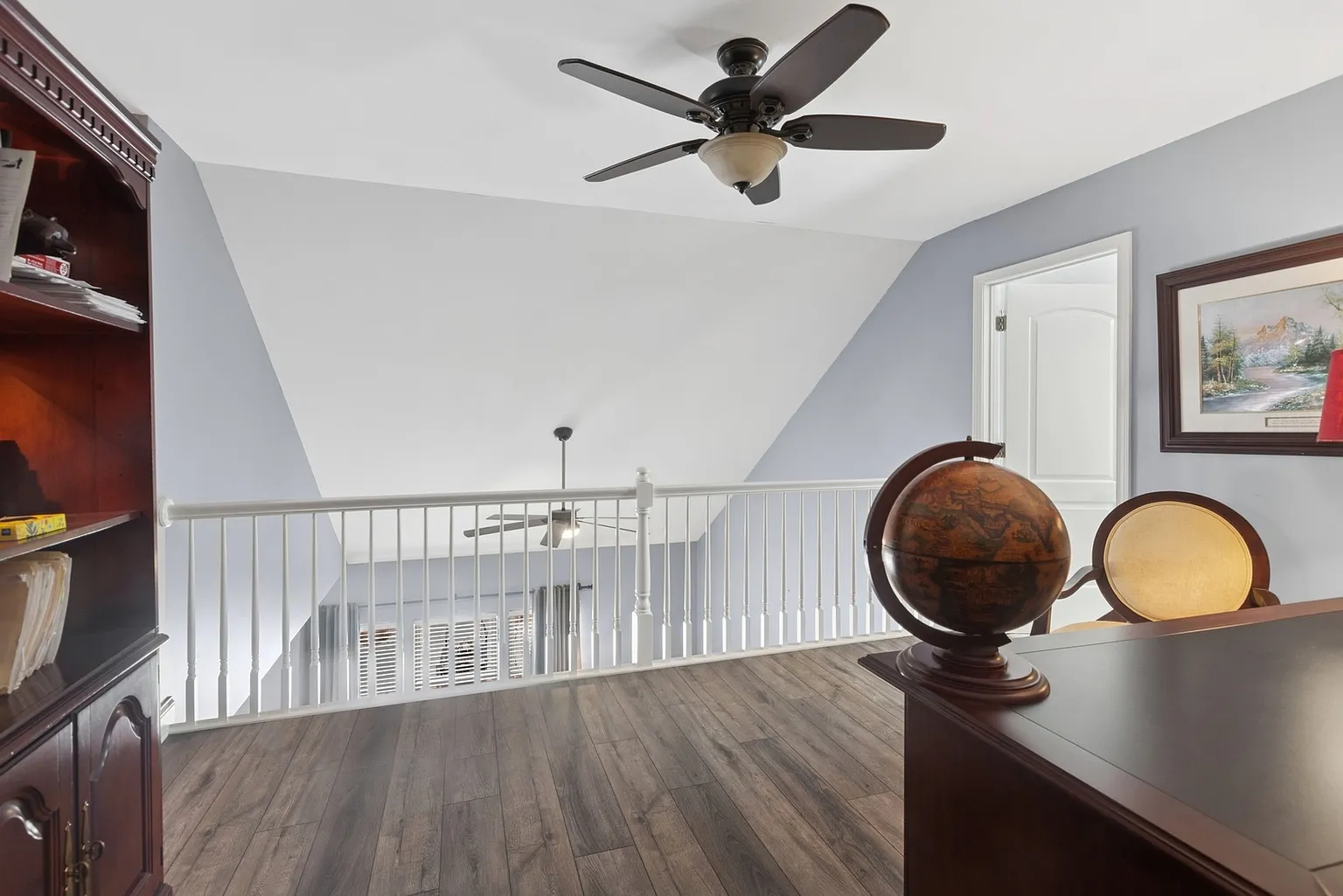 Well-lit interior with ceiling fan, wood flooring, railing, and open living space