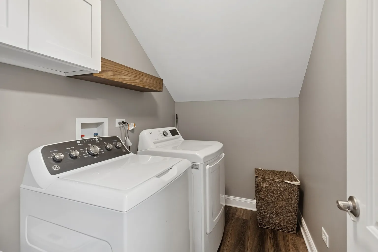 Laundry room with washer, dryer, gray walls, wooden shelf, and basket.