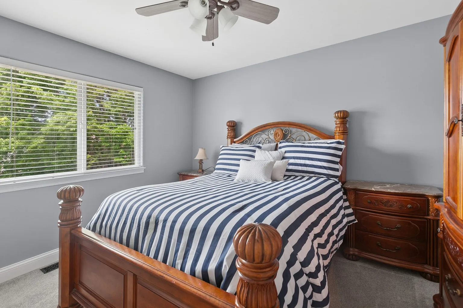 Bedroom with wooden bed frame, striped bedding, window blinds, and wooden dresser.