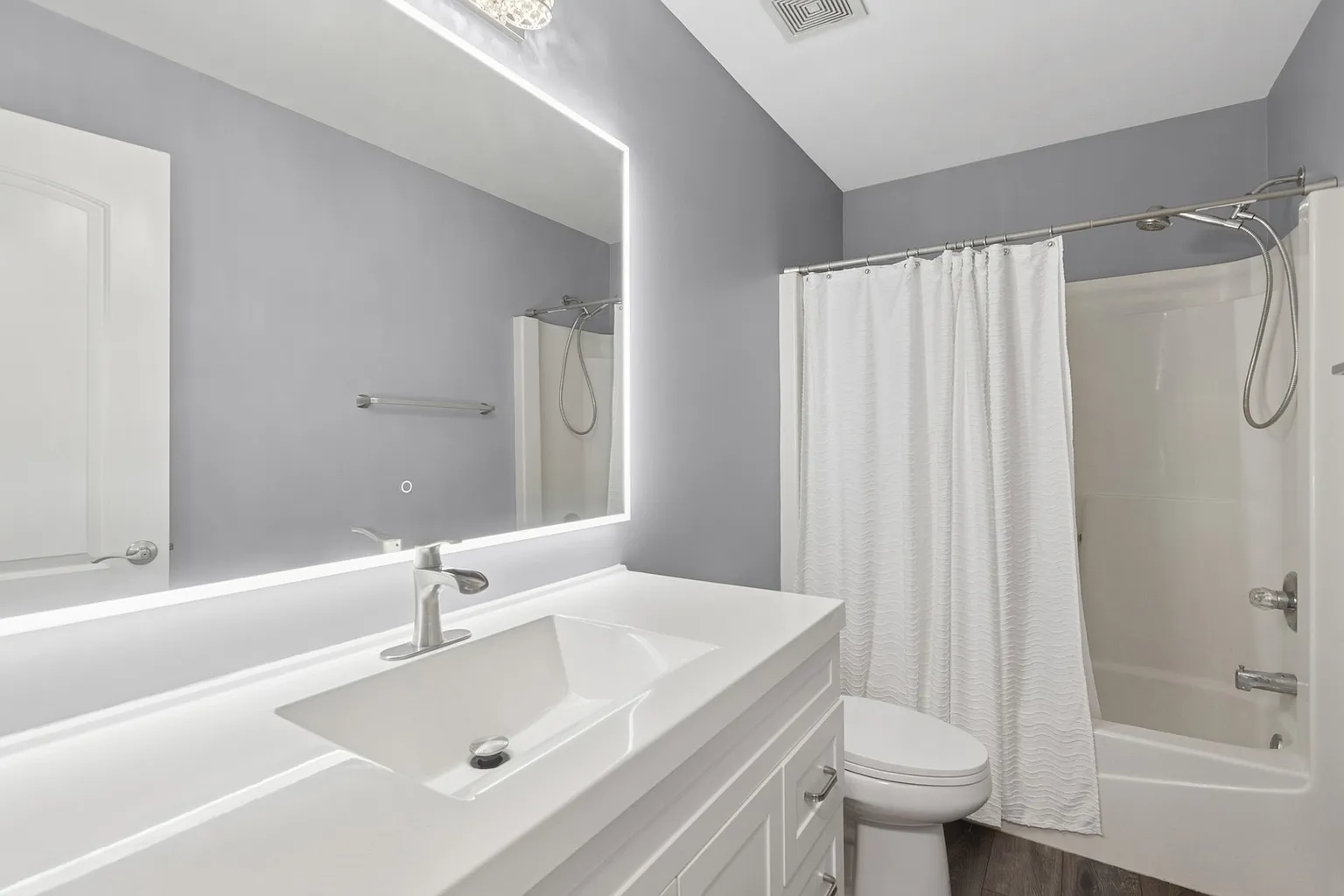 Modern bathroom with LED mirror, white vanity, toilet, and bathtub shower combo.