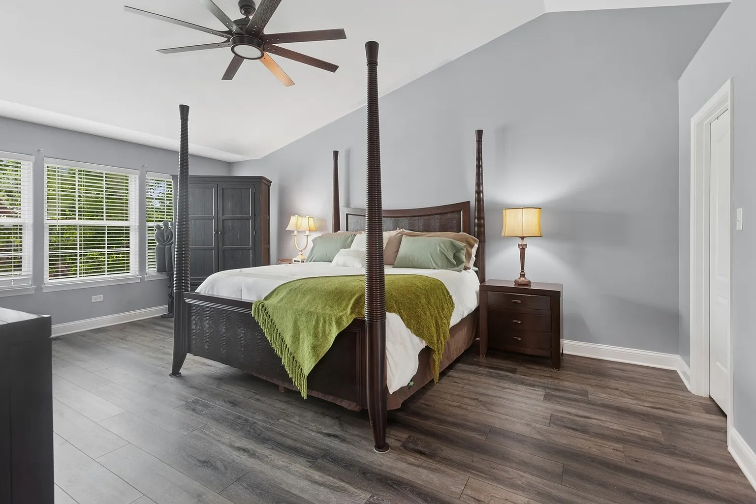 Modern bedroom with four-poster bed, green throw blanket, dark wood furniture, and hardwood floors.