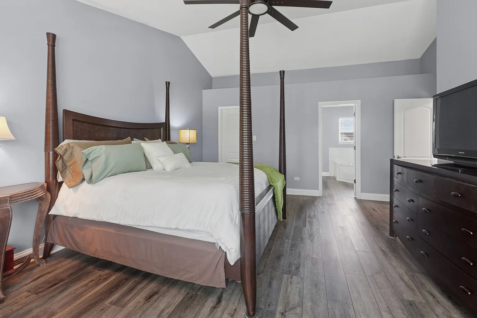Spacious bedroom with four-poster bed, blue walls, hardwood floors, dresser, and TV.