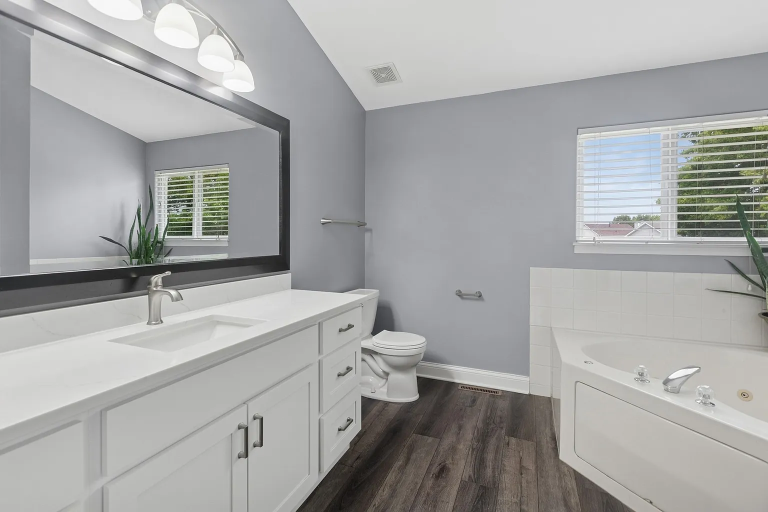 Modern bathroom with double vanity, large mirror, toilet, bathtub, and gray walls.