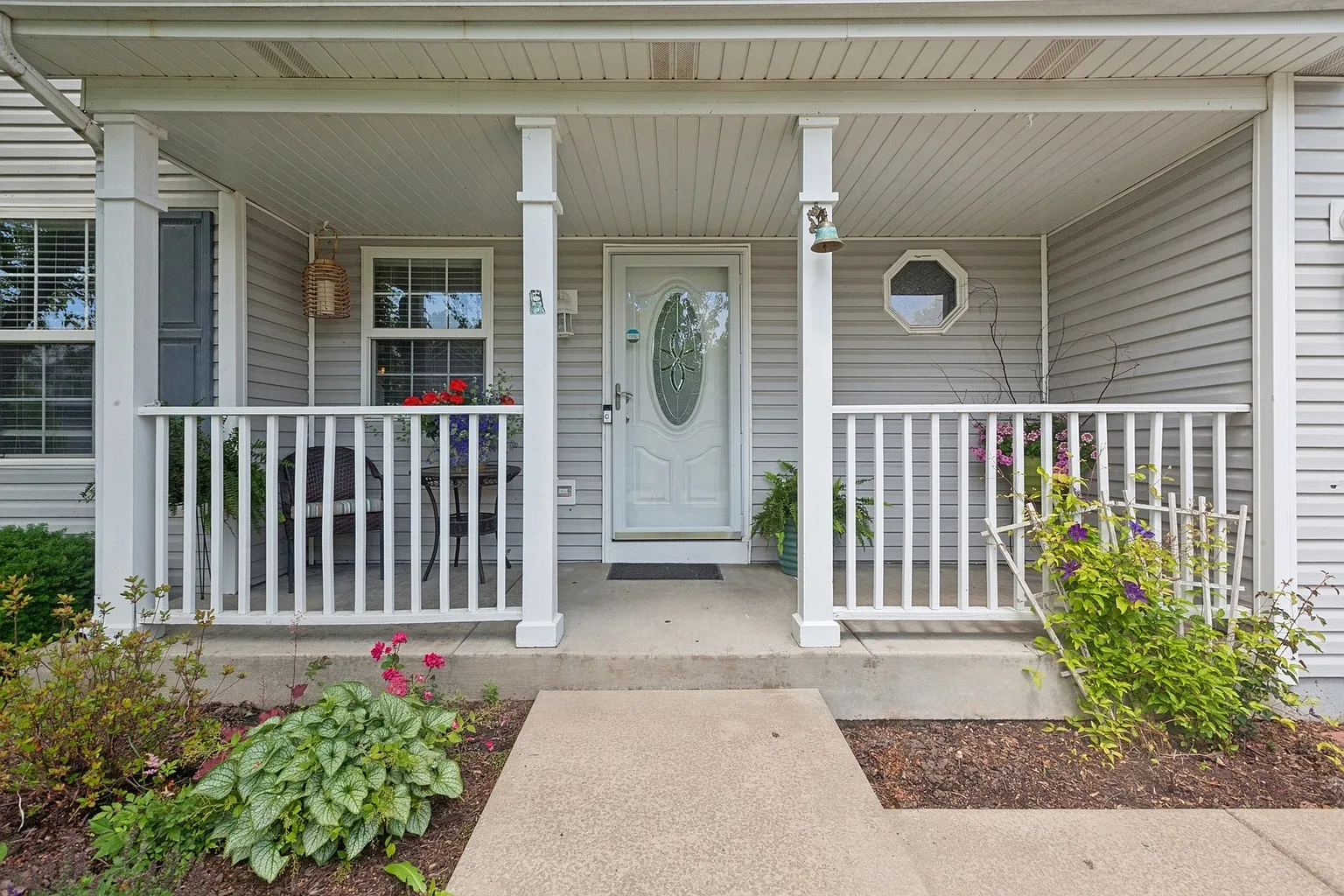 Front porch with white railings, decorative glass door, and potted plants.