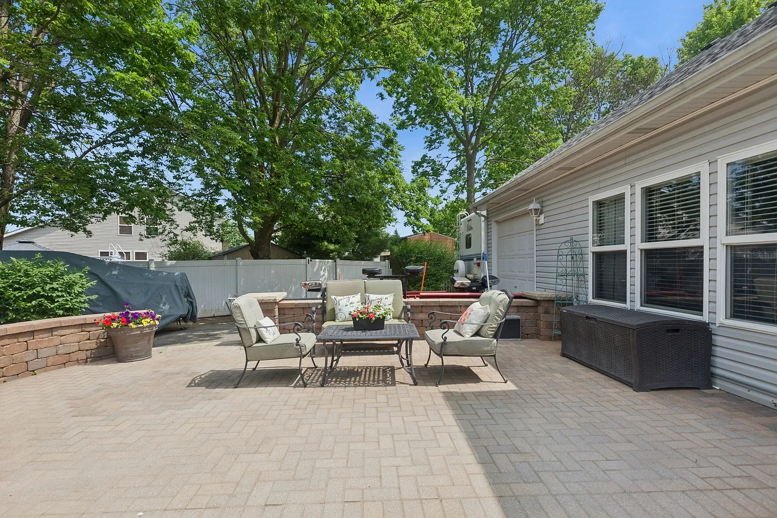 Spacious outdoor patio with seating, flower table, green trees, and bushes.