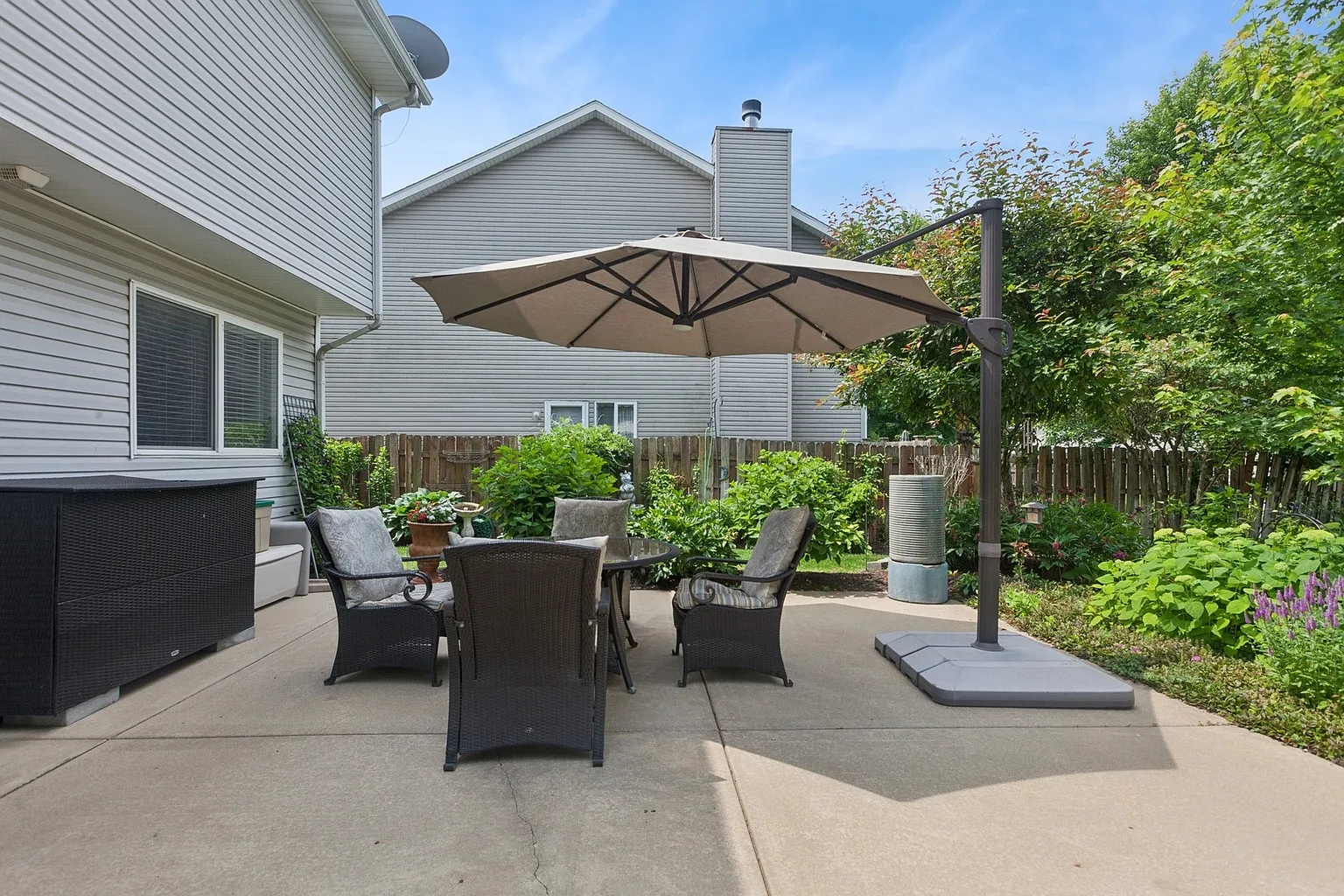 Patio with table, chairs, umbrella, greenery, and plants.