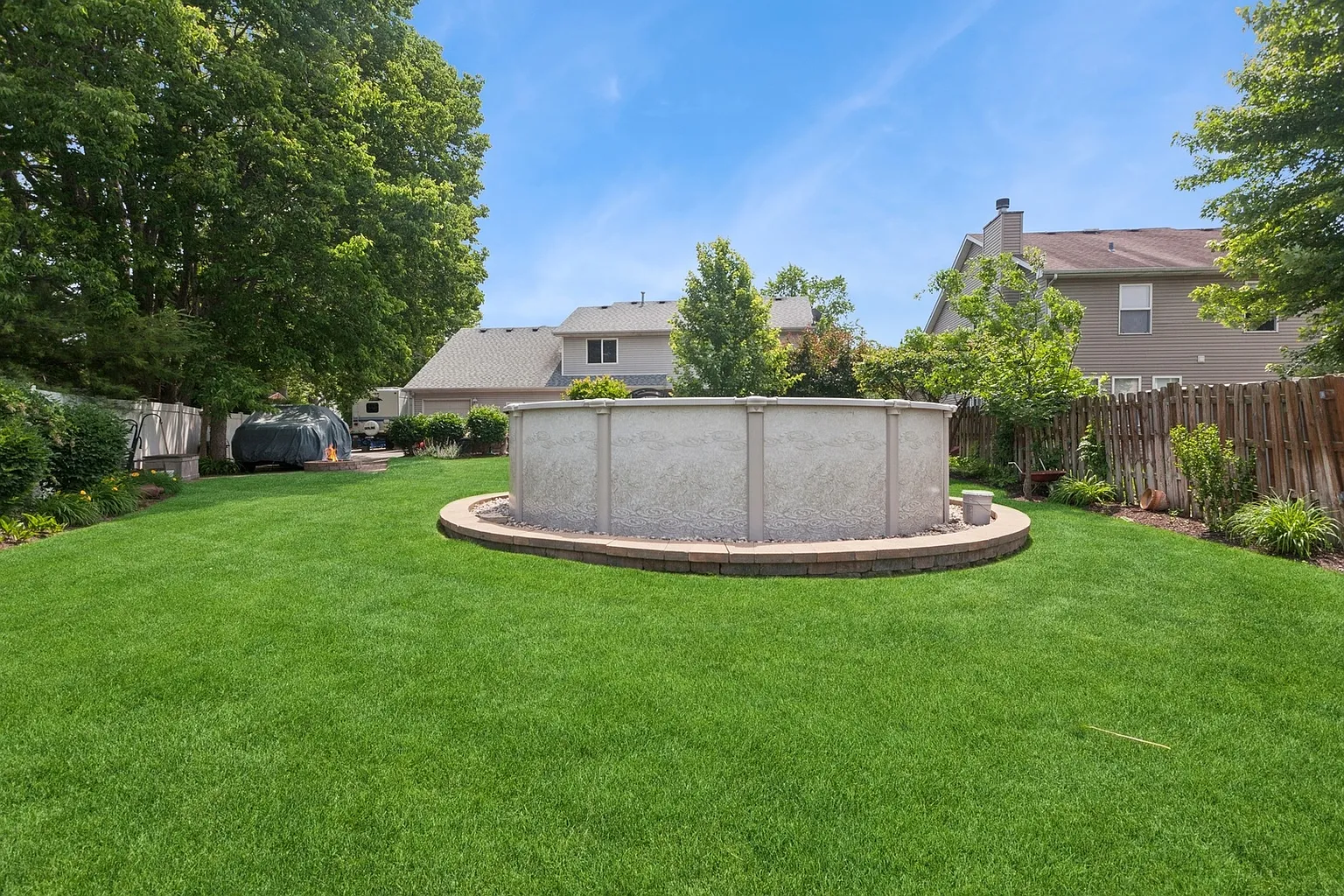 Backyard with above-ground pool, green lawn, trees, and houses in the background.