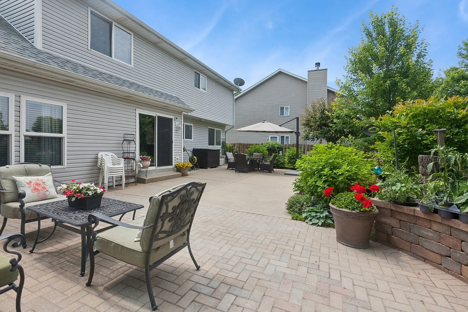 Backyard patio with seating, table, potted plants, and greenery.