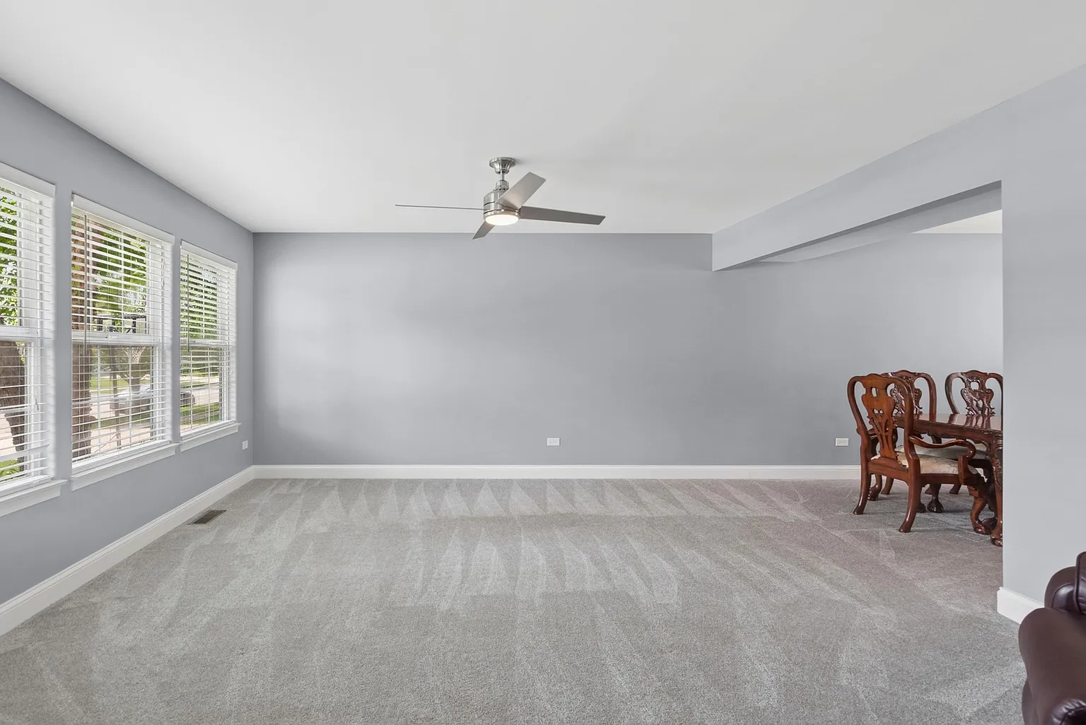Spacious room with gray walls, ceiling fan, large windows, and dining area.