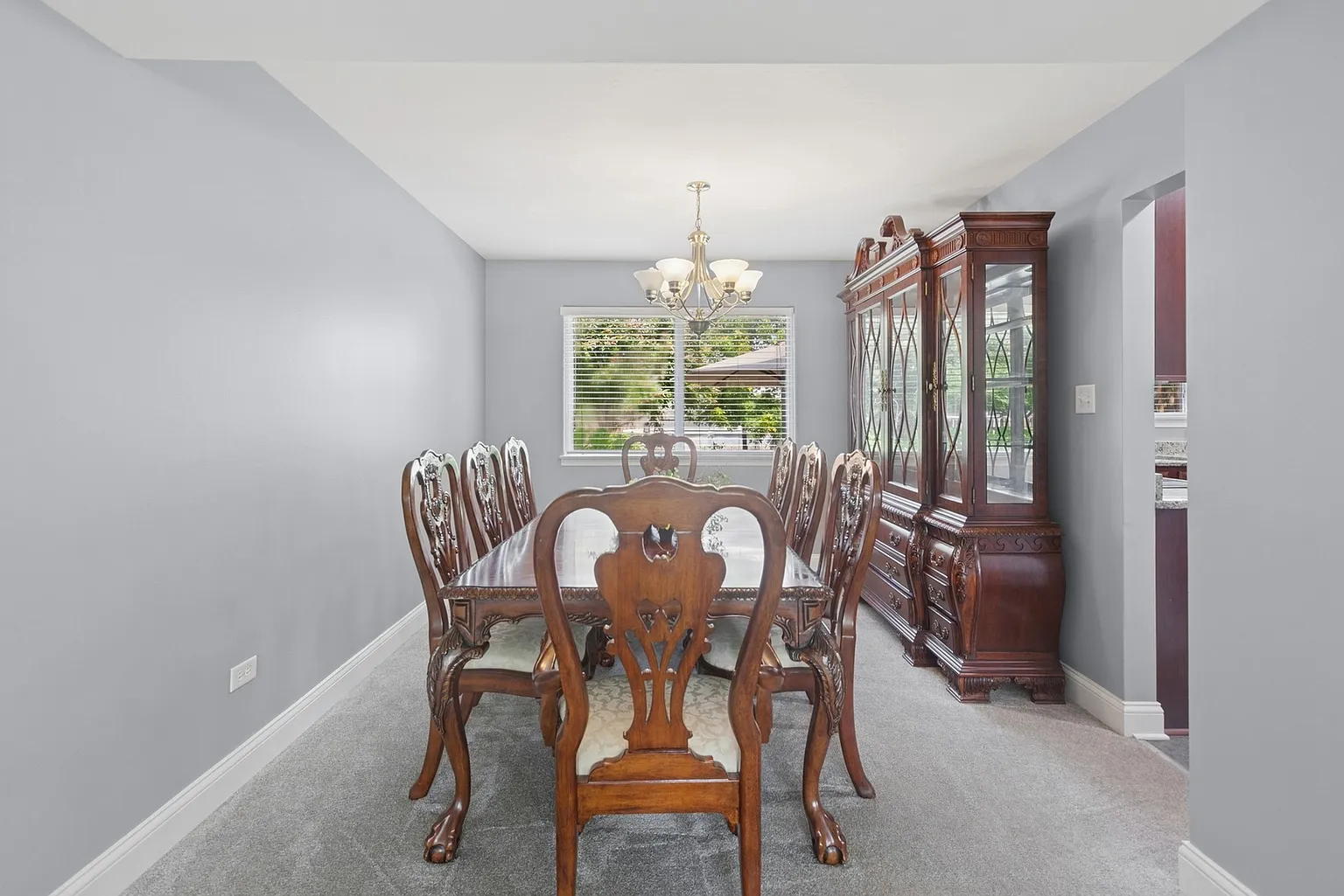 Dining room with wooden table, chairs, chandelier, china cabinet, and windows.
