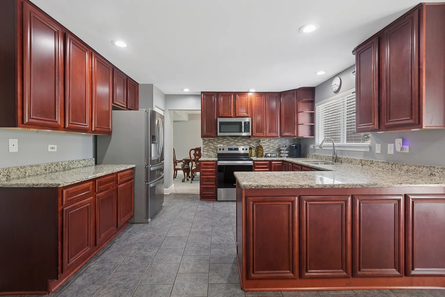 Modern kitchen with dark wood cabinets, granite countertops, stainless appliances, and tile floor.