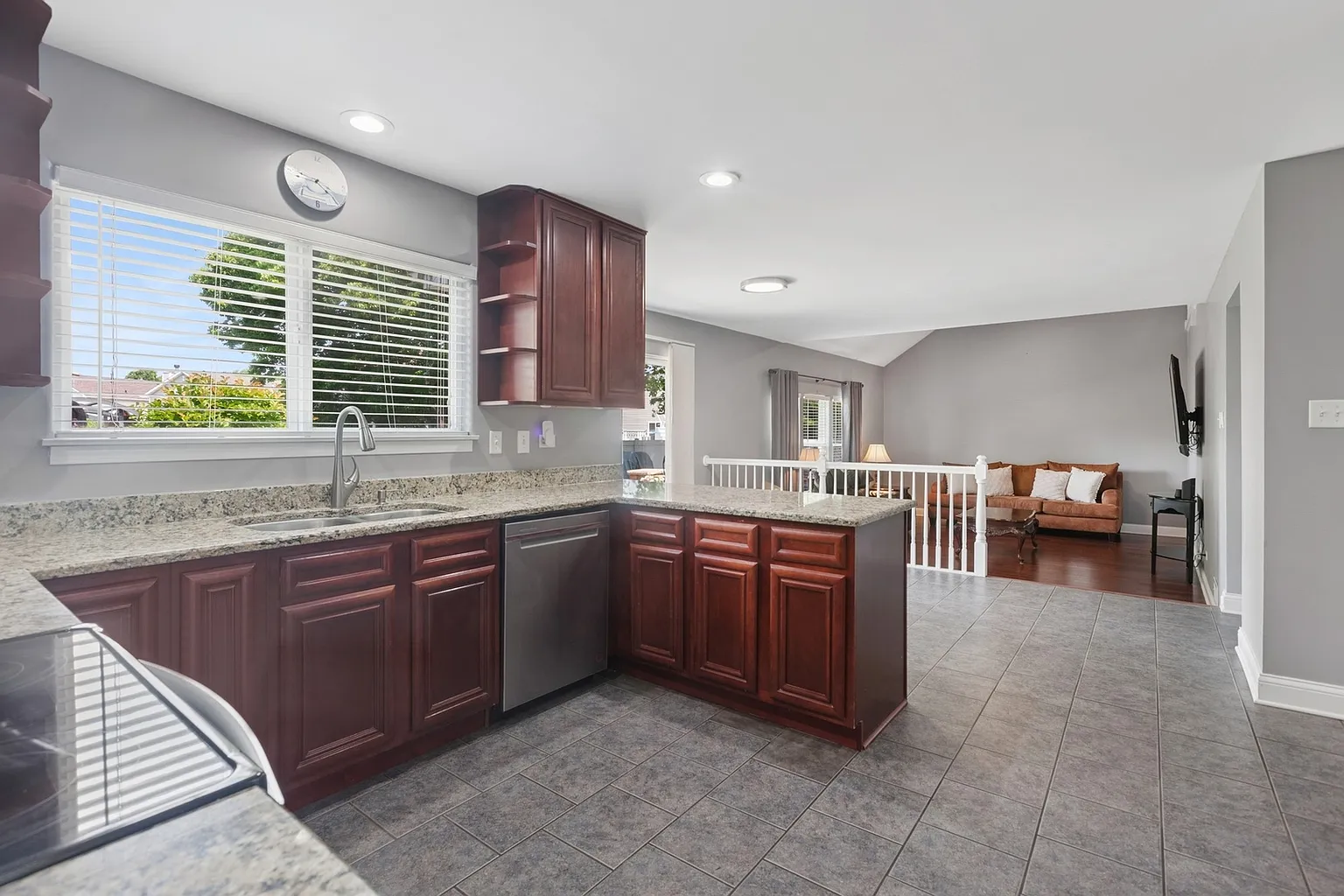 Modern kitchen with dark wood cabinets, granite counters, stainless appliances, and natural light.