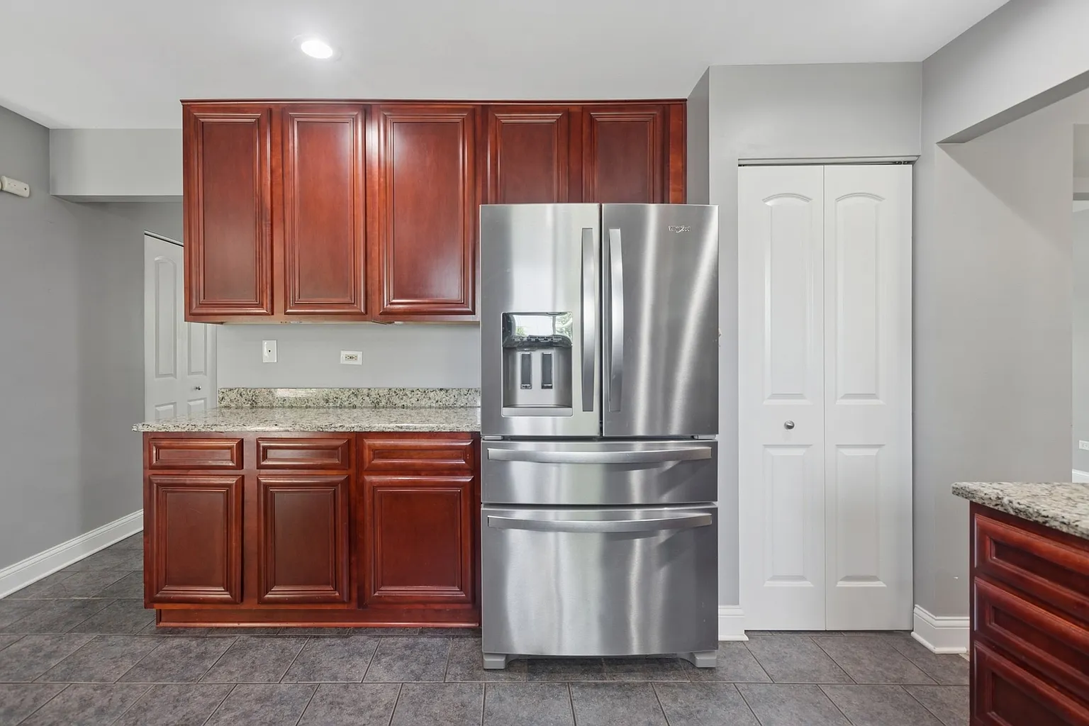 Modern kitchen with dark wood cabinets, stainless steel fridge, and granite countertops.