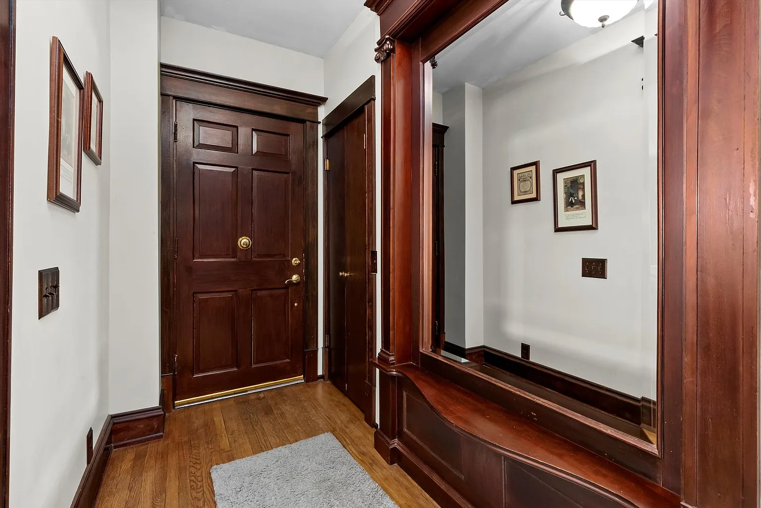 Hallway with wooden door, framed mirror, wall pictures, and small floor mat.