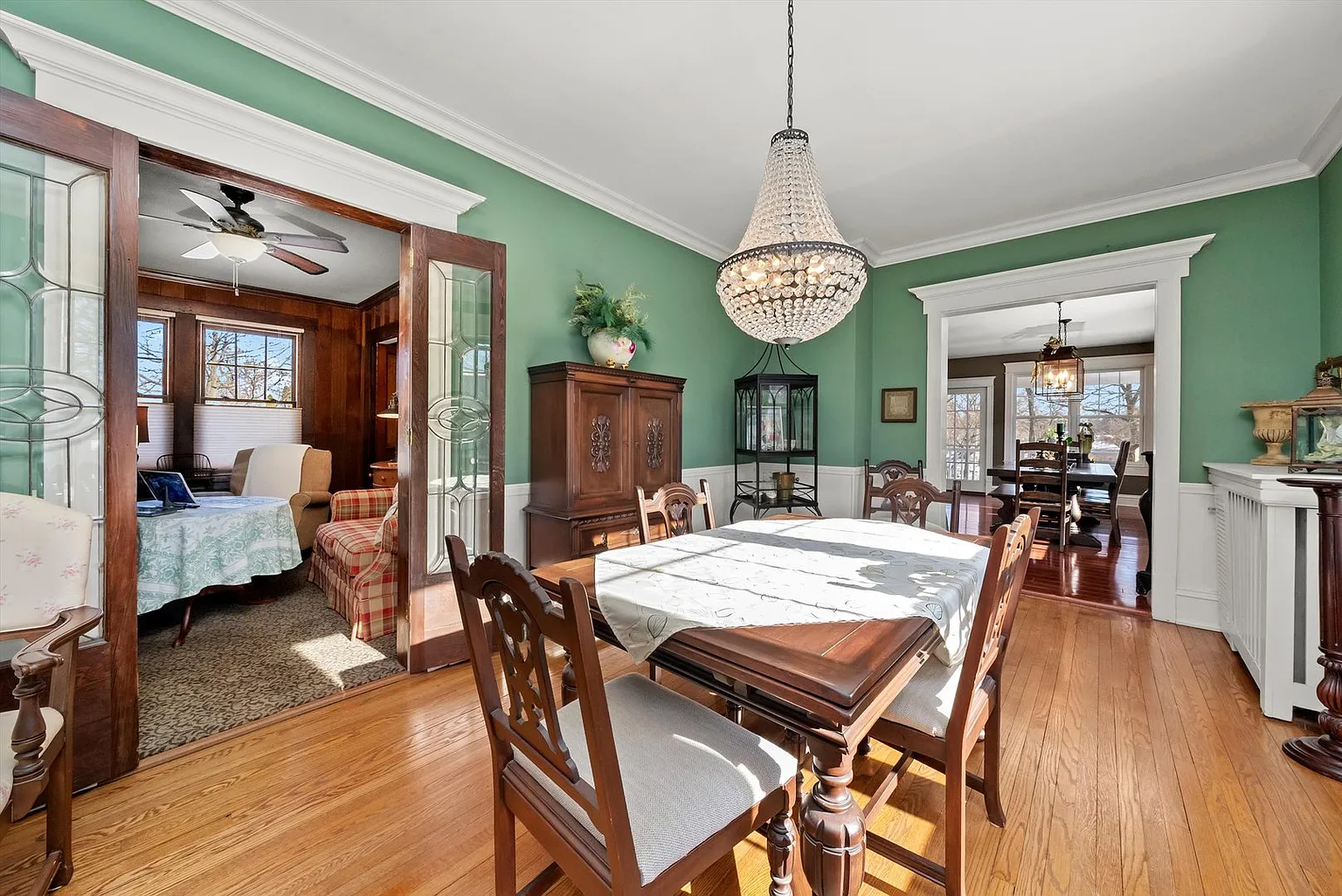 Dining area with wooden table, chairs, green walls, hardwood floors, and chandelier.