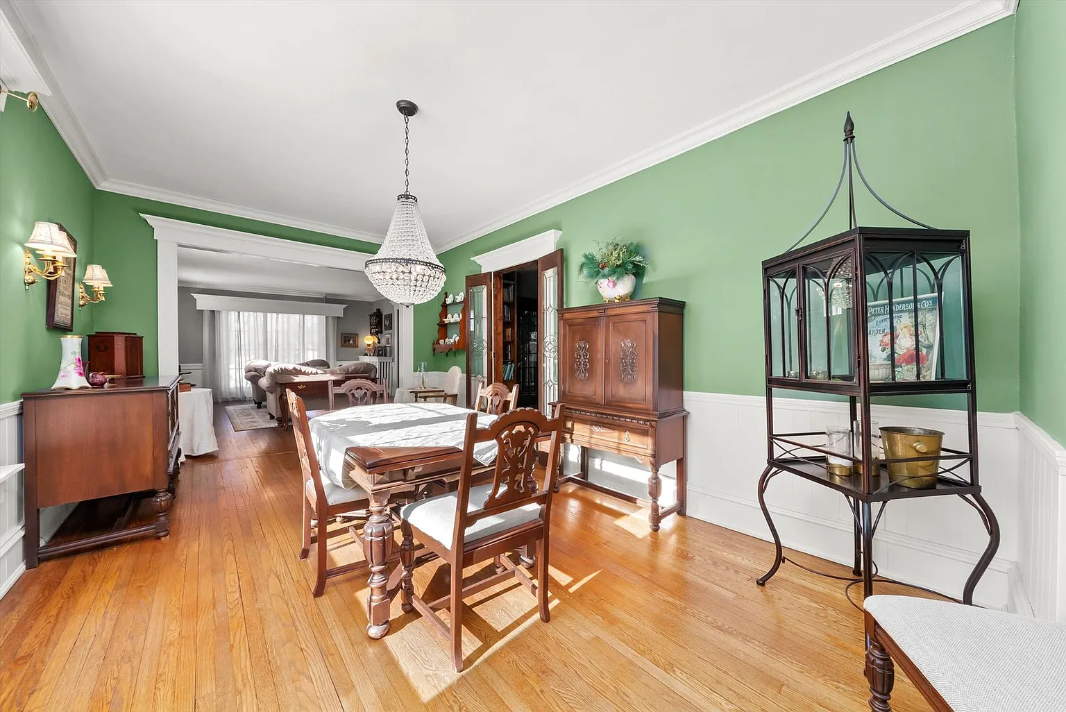 Dining room with green walls, hardwood floors, chandelier, six-seat table, and glass cabinet.