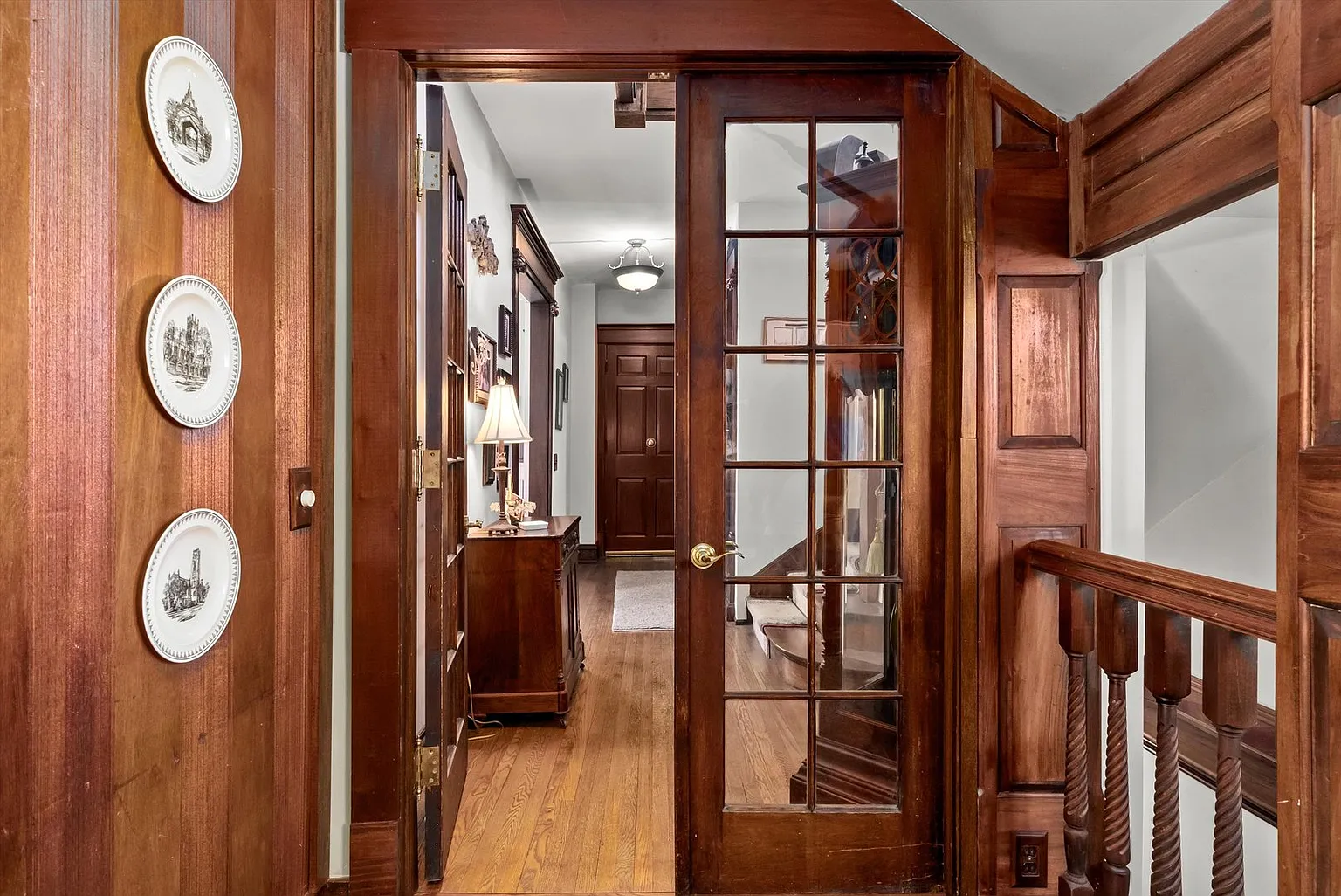Wooden hallway with glass door, wall decor, and wooden railings.