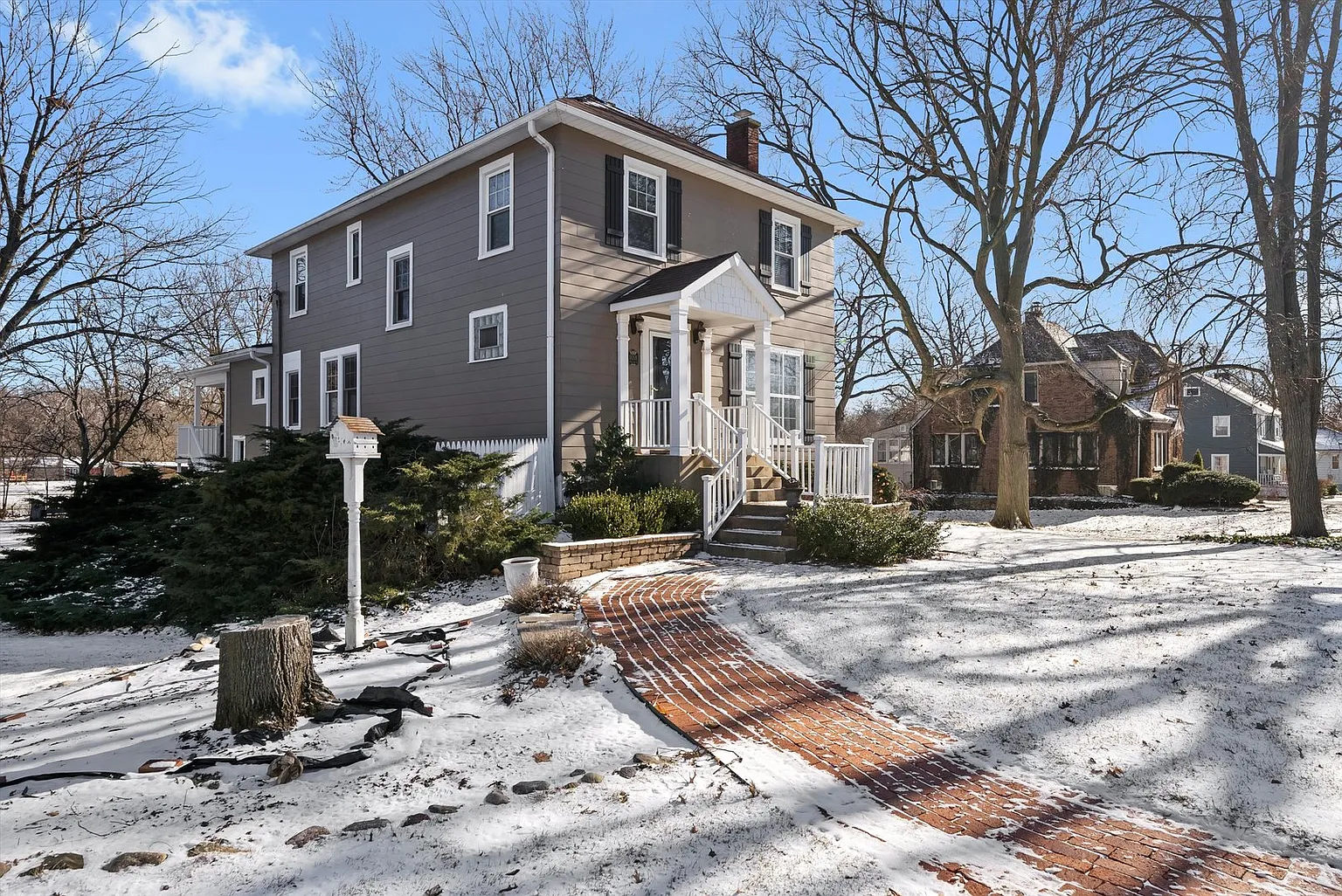Two-story house with white trim, brick path, snowy trees, and sunny winter atmosphere.
