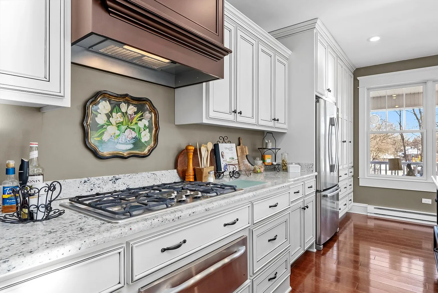 Modern kitchen with white cabinetry, granite counter, gas stove, stainless steel appliances, and bright natural light.