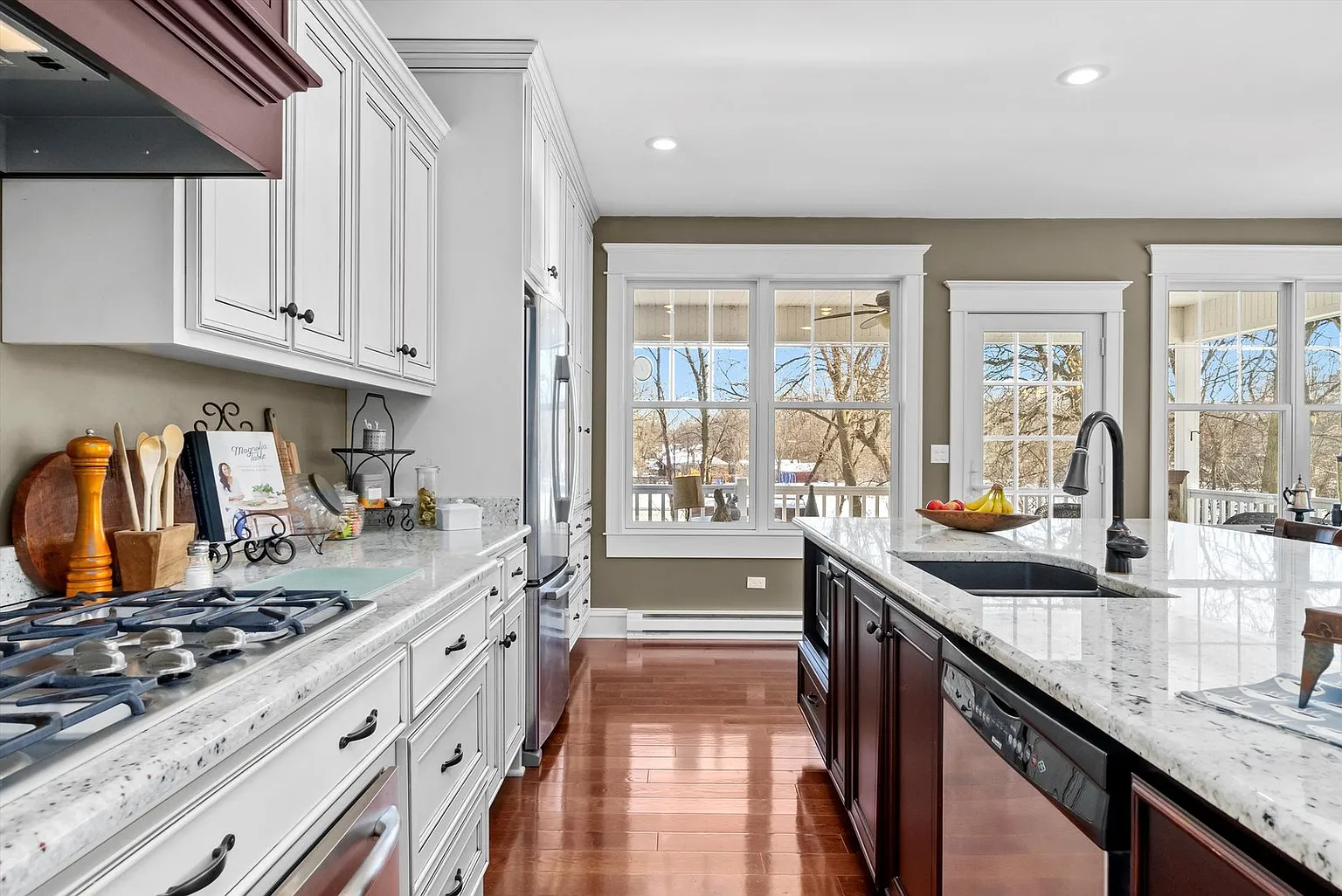 Modern kitchen with white cabinets, granite countertop, gas stove, stainless appliances, and natural light.