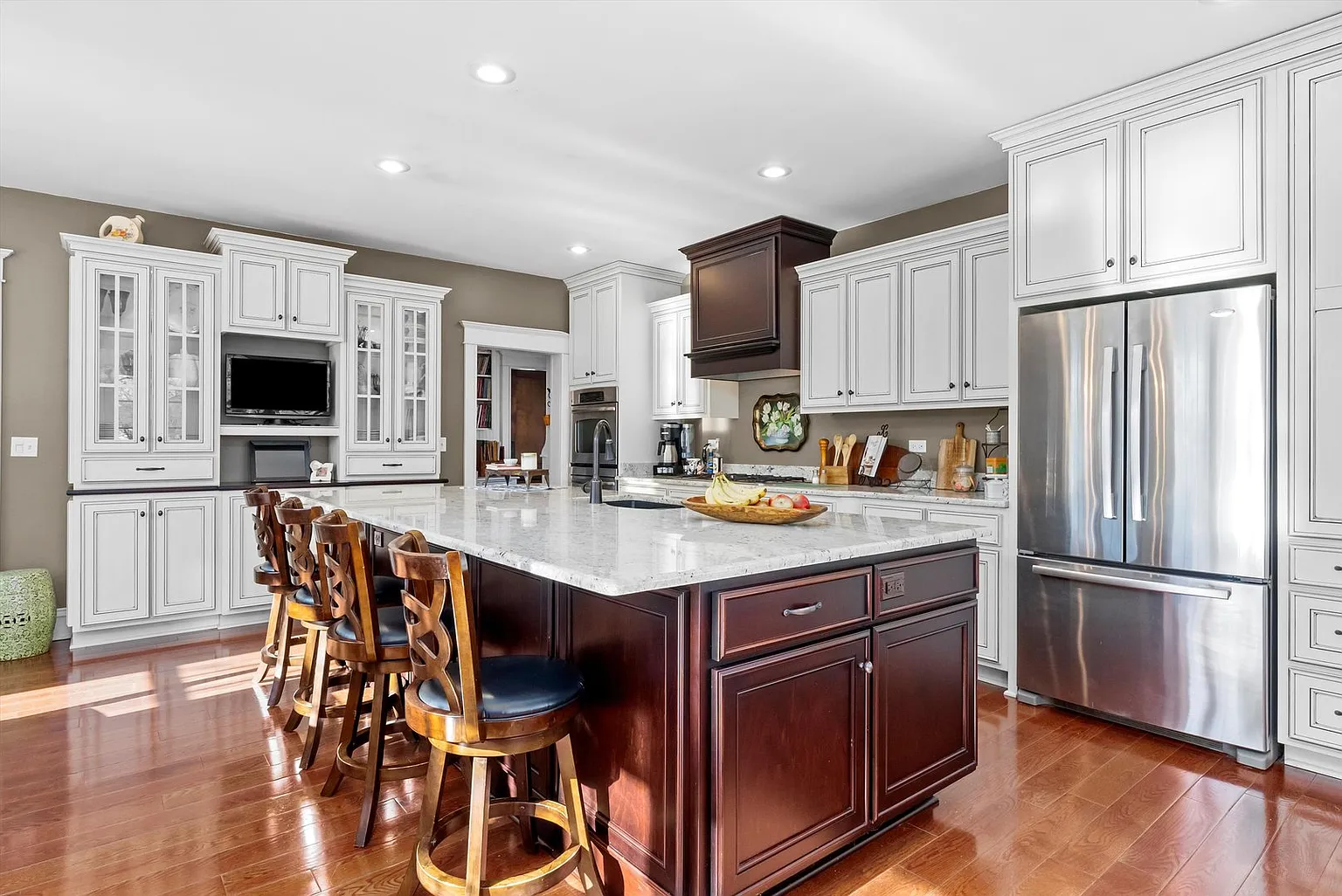Modern kitchen with marble island, dark wood cabinets, light walls, and large windows.