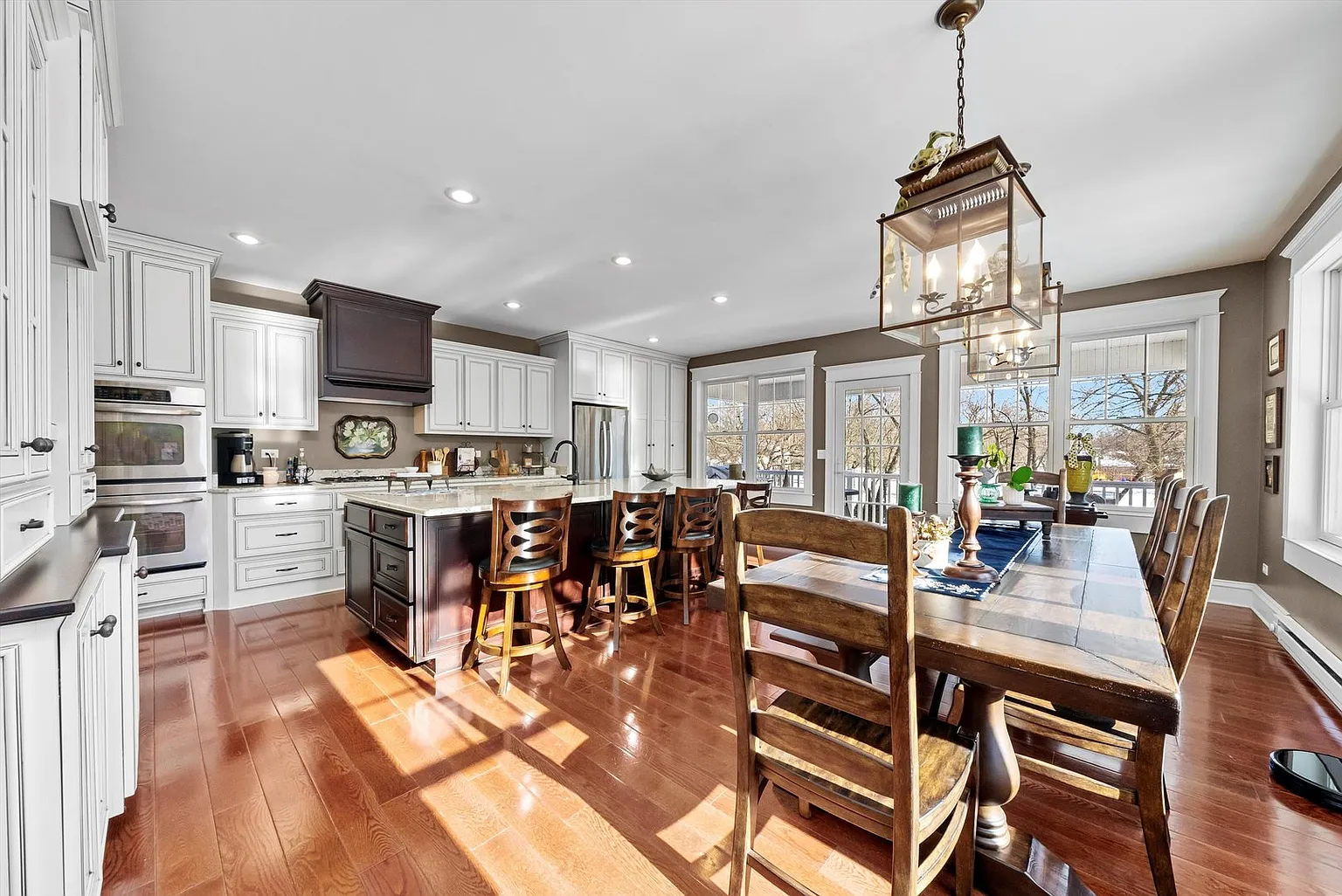 Modern kitchen with white cabinets, stainless appliances, wooden dining table, hardwood floors, and pendant lights.