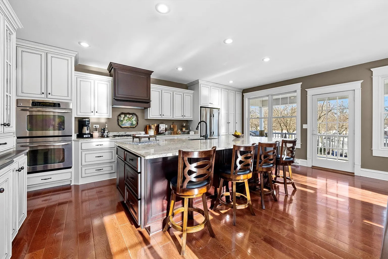 Modern kitchen with white cabinets, wooden dining table, and bright natural light.