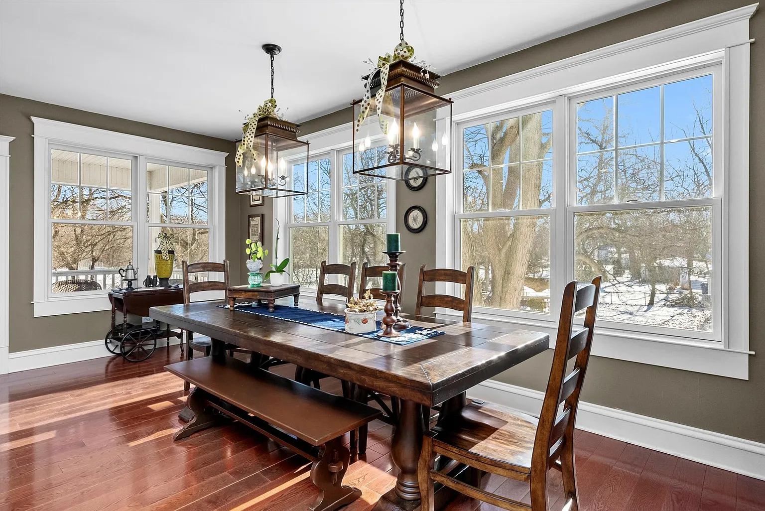Spacious dining room with wooden table, chairs, green walls, pendant lights, and snowy view.