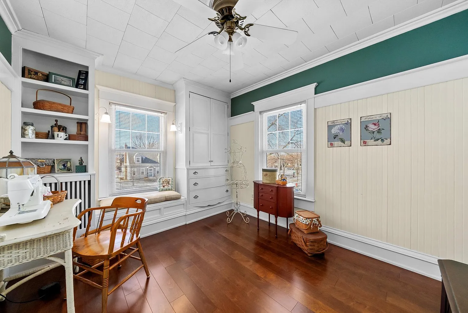 Cozy room with window seat, red cabinet, wood floor, white and green walls, table, chairs, and shelves.