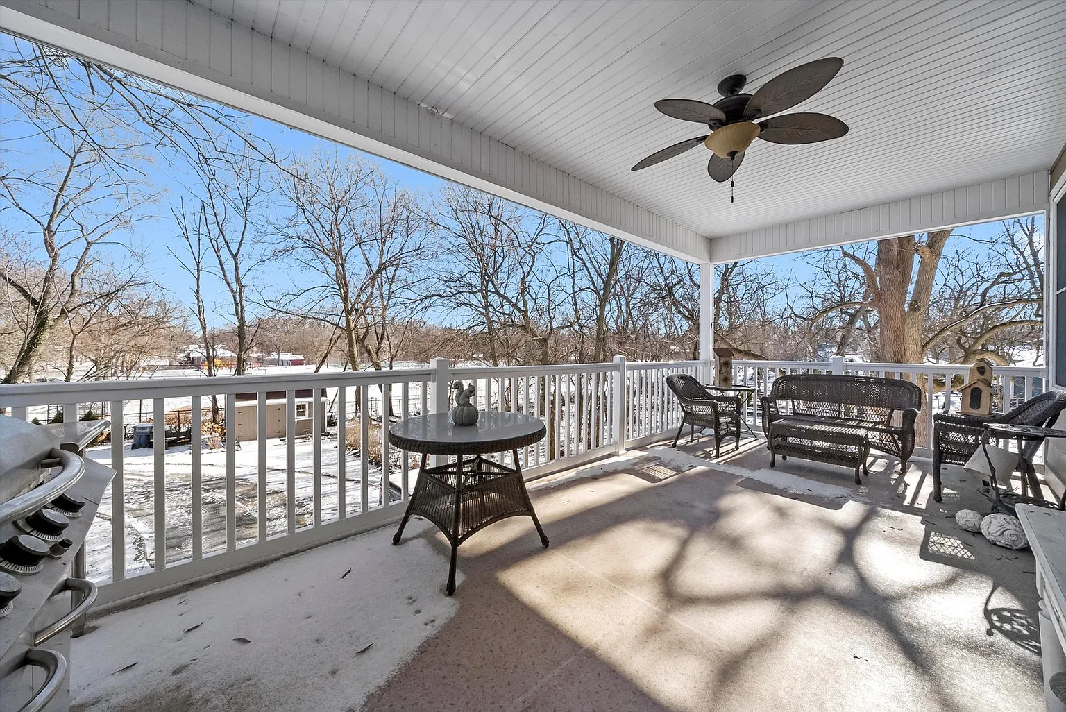 Covered porch with ceiling fan, round table, seating, trees, and blue sky.