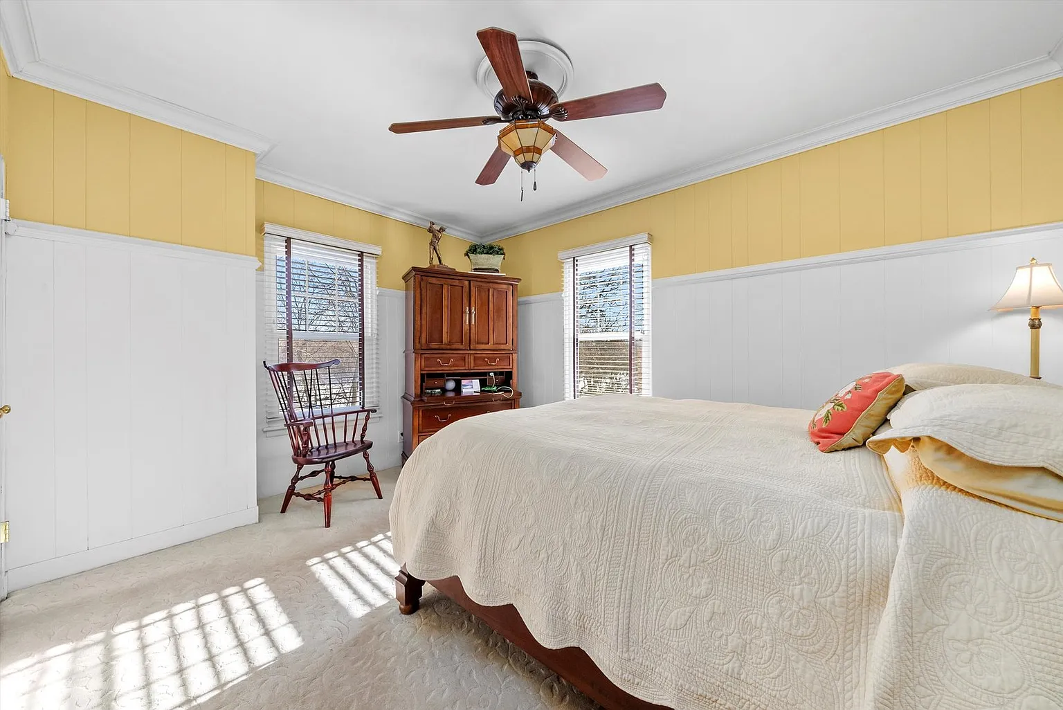Cozy bedroom with bed, light quilt, wooden chair, yellow walls, and natural light.