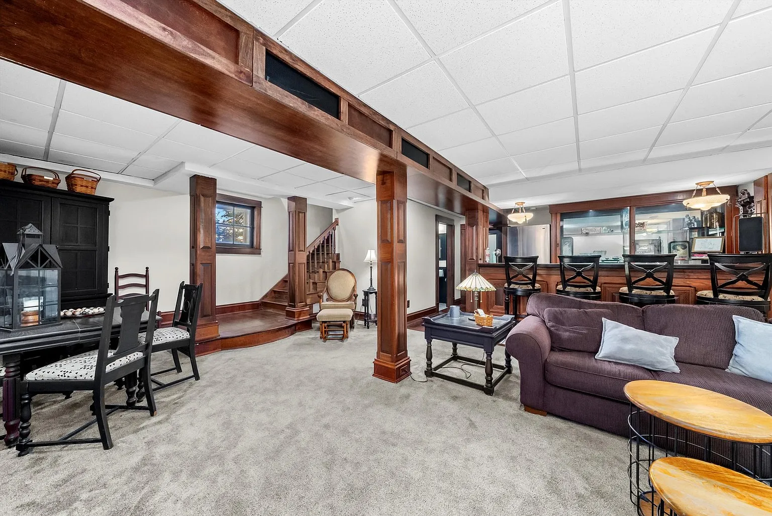 Spacious carpeted living area with dining table, staircase, couch, and natural light.