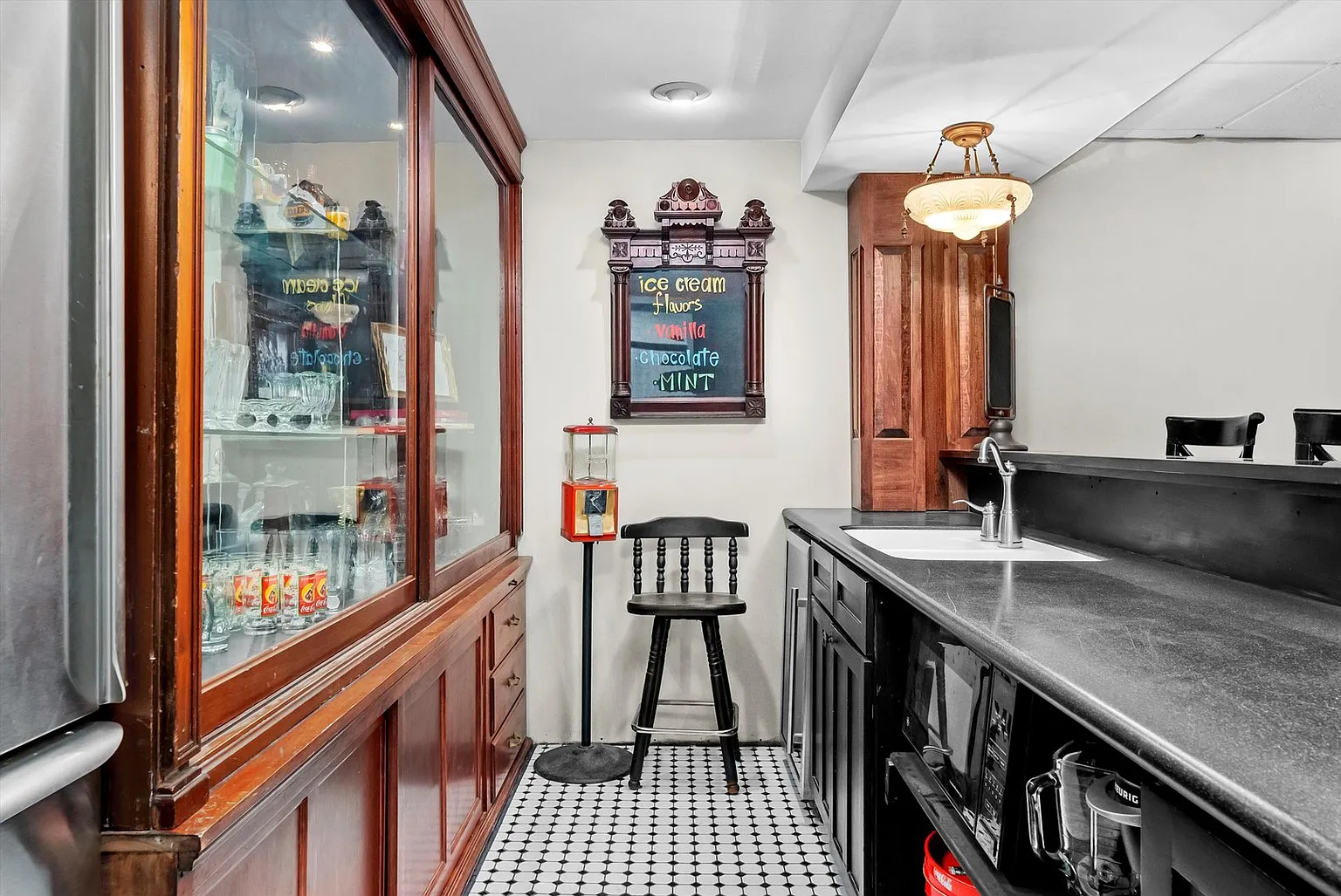 Room with bar counter, glass cabinets, drinkware, chair, wall sign, and checkered floor.