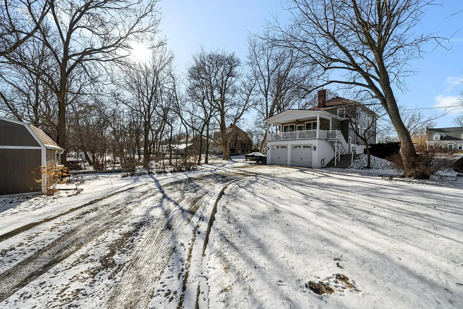 Snow-covered yard with tire tracks, house, bare trees, and long winter shadows.