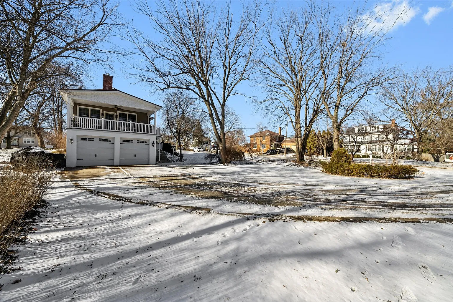 Two-story house with double garage in snowy yard, bare trees, and clear blue sky.
