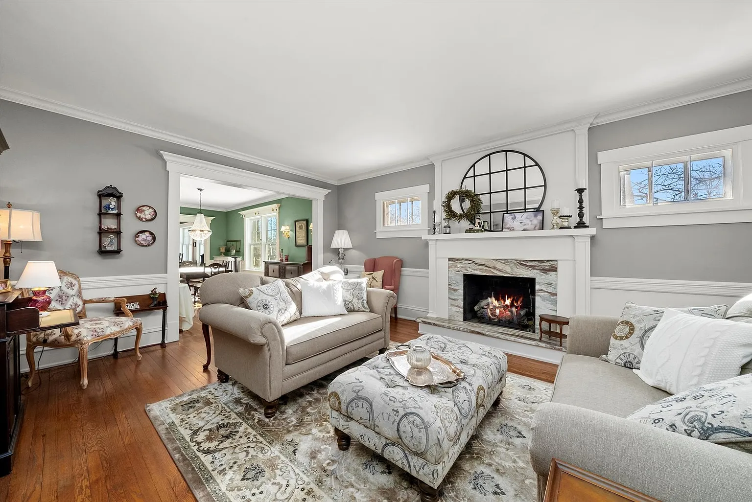 Warm living room with gray walls, beige sofas, ottoman, fireplace, and dining area.