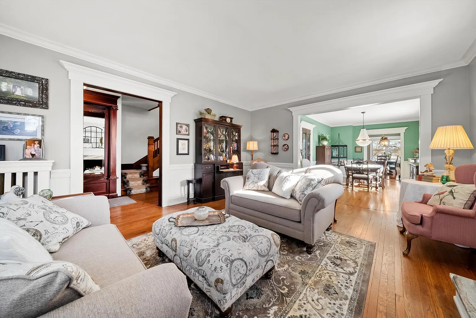 Bright living room with gray walls, hardwood floors, beige sofa, rug, and wooden cabinet.