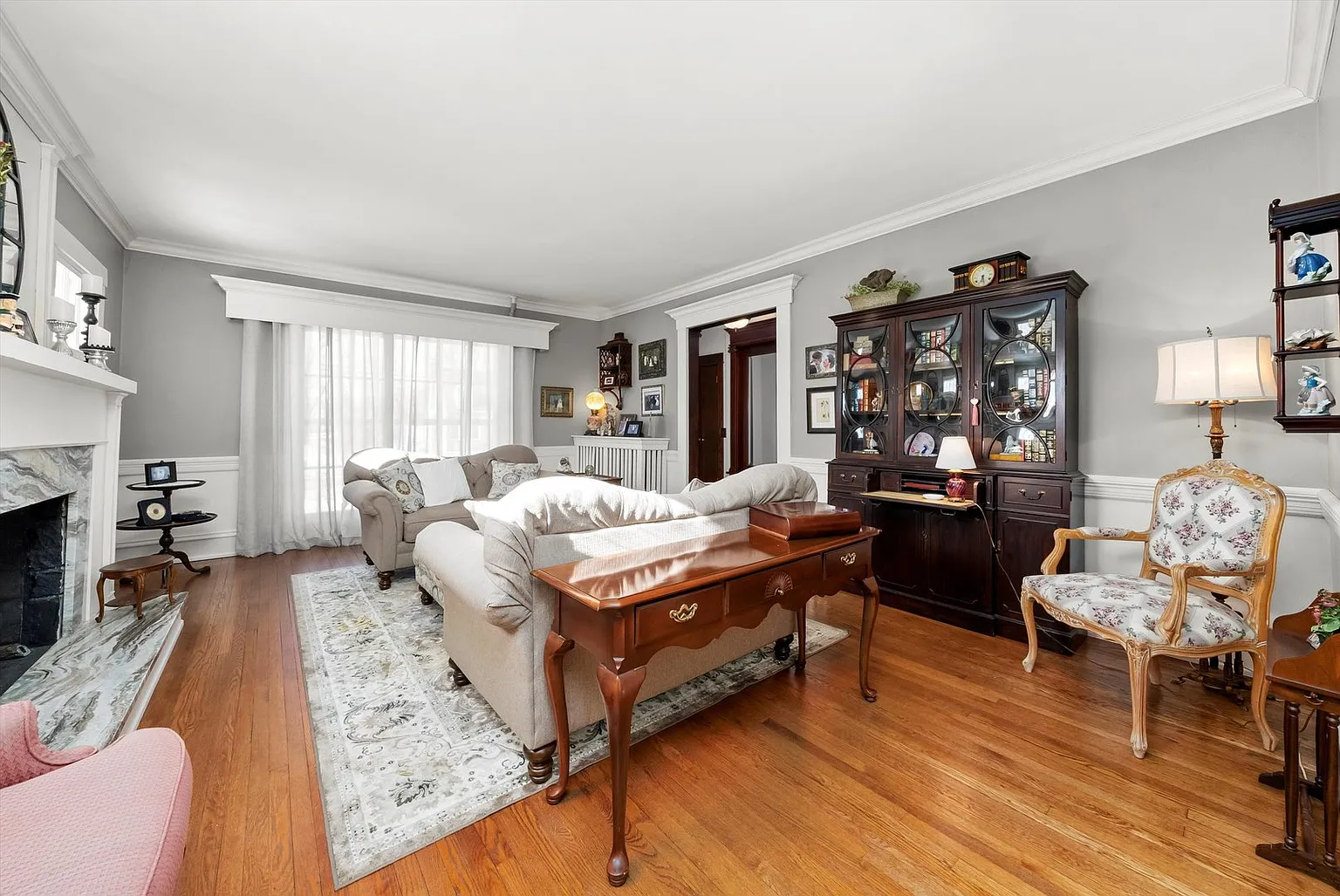 Cozy living room with beige sofa, wood cabinet, marble fireplace, and large window drapes.