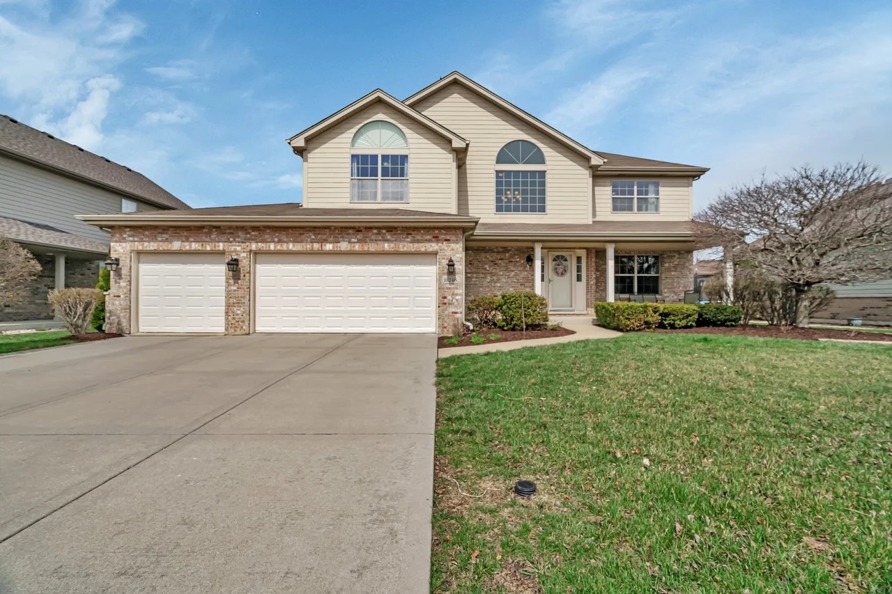 Two-story suburban house with brick accents, arched windows, garage, and lawn.