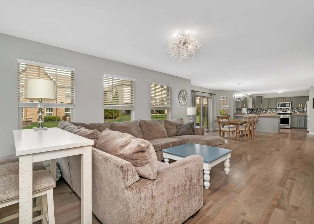 Open living room with sectional sofa, chandelier, large windows, and hardwood floors.