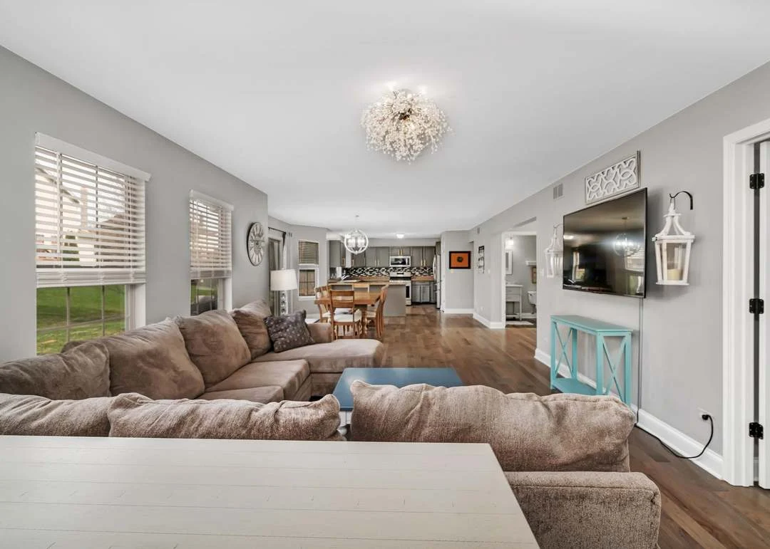 Modern living room with sectional sofa, open kitchen, dining area, and chandelier.