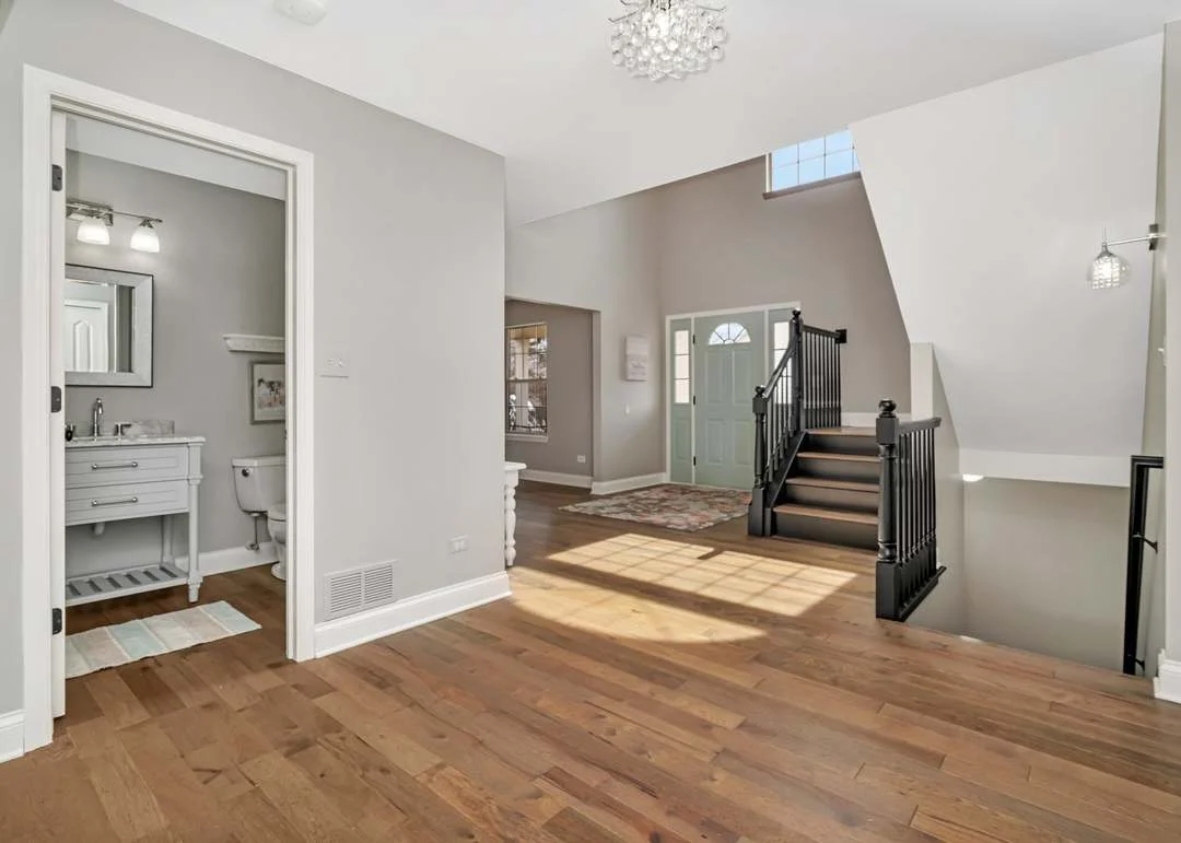 Spacious entryway with wooden floors, teal door, black railing, and white vanity.